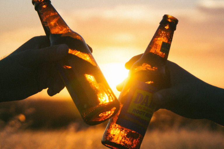 Season Closing Party Zwei Hände stoßen mit Bierflaschen gegen den Sonnenuntergang an.