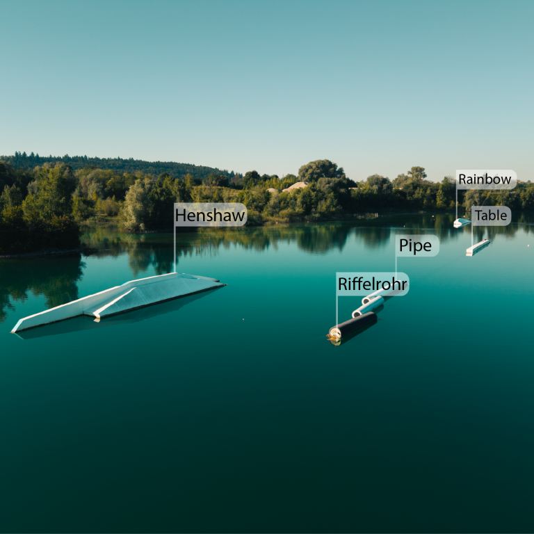 Hindernisse im Wakepark Pfullendorf Blick auf einen ruhigen See mit schwimmenden Objekten und Beschriftungen für Aktivitäten.