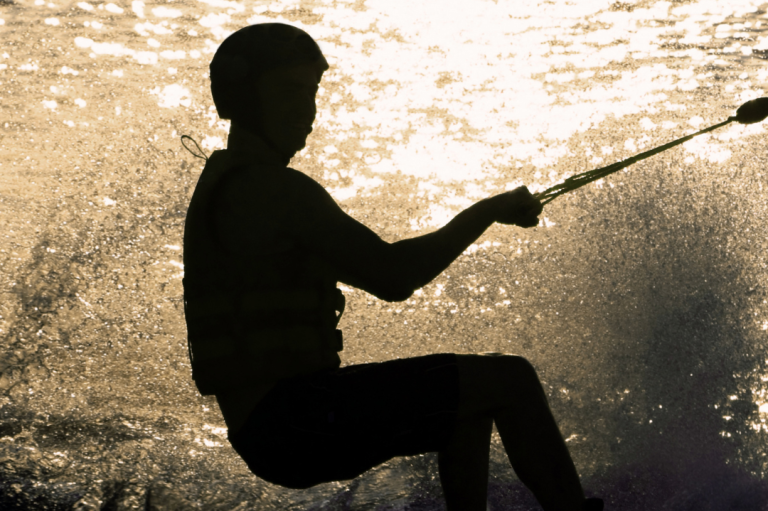 Event 'Schier Boards Testtag' Person beim Wakeboard fahren, silhouettiert vor einem glitzernden Wasserhintergrund.