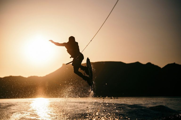 Happy Hour Ein Wakeboarder springt über das Wasser vor einem Sonnenuntergang.