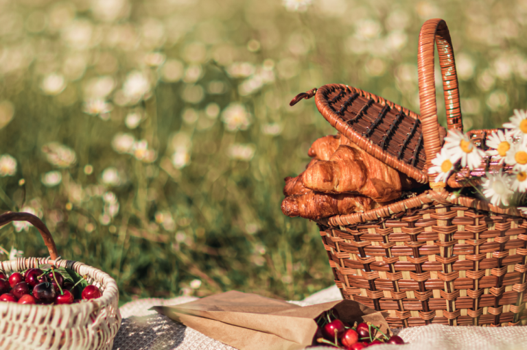 Midsommar Special Ein Weidenkorb mit frischen Croissants und Blumen auf einer Wiese.