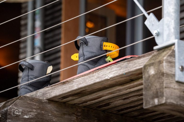 Sportstunde am See Schwarze Schuhe mit gelbem Zubehör stehen auf einem Holzregal.