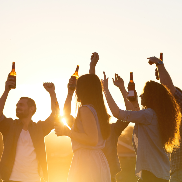 Gruppenevent im Freien bei Sonnenuntergang, Menschen halten Bierflaschen hoch.