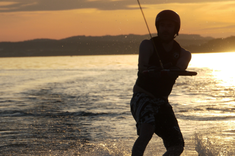 Sportstunde am See Person wakeboardet bei Sonnenuntergang auf ruhigem Wasser.