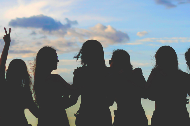 Female Only Event Silhouetten von sechs Frauen bei Sonnenuntergang, einige zeigen das Friedenszeichen.