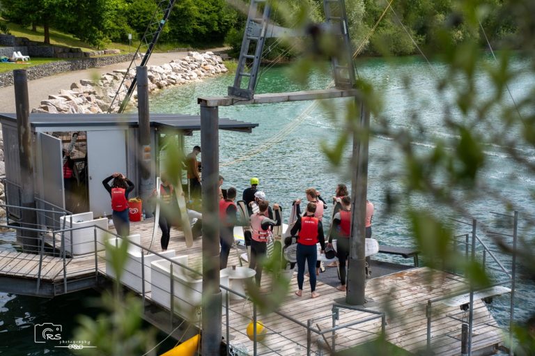 Volleyballturnier Gruppe von Menschen in roten Westen am Ufer eines Gewässers, umgeben von Bäumen.