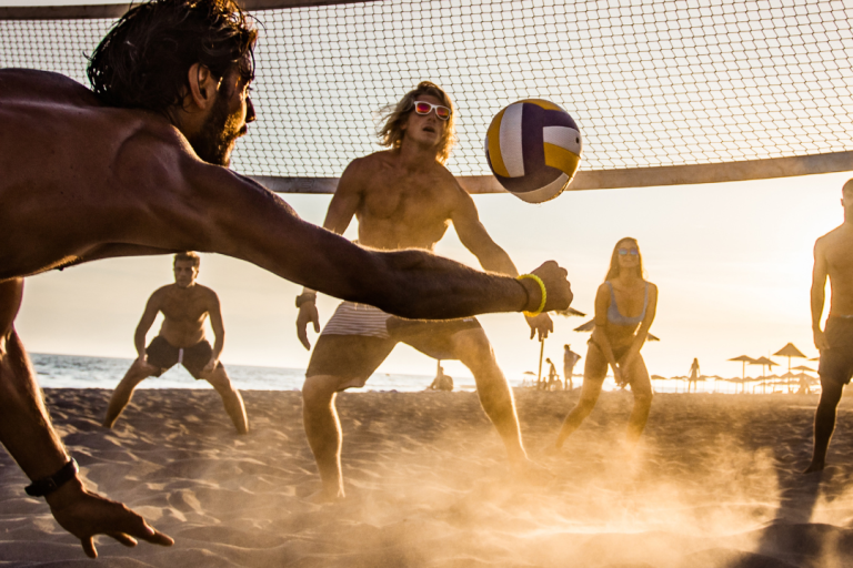 Volleyballturnier Männer und Frauen spielen Beachvolleyball bei Sonnenuntergang am Strand.