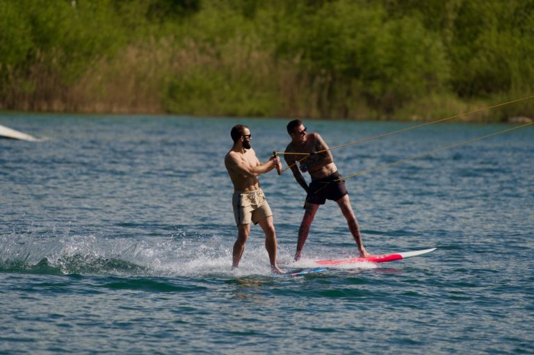Seifenkistenrennen Zwei Männer paddeln auf einem See, einer hilft dem anderen auf einem Paddleboard.