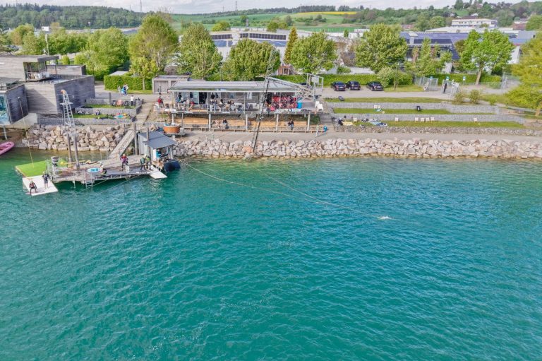 Seifenkistenrennen Uferbereich mit Booten, Holzsteg und begrünten Flächen am Wasser.