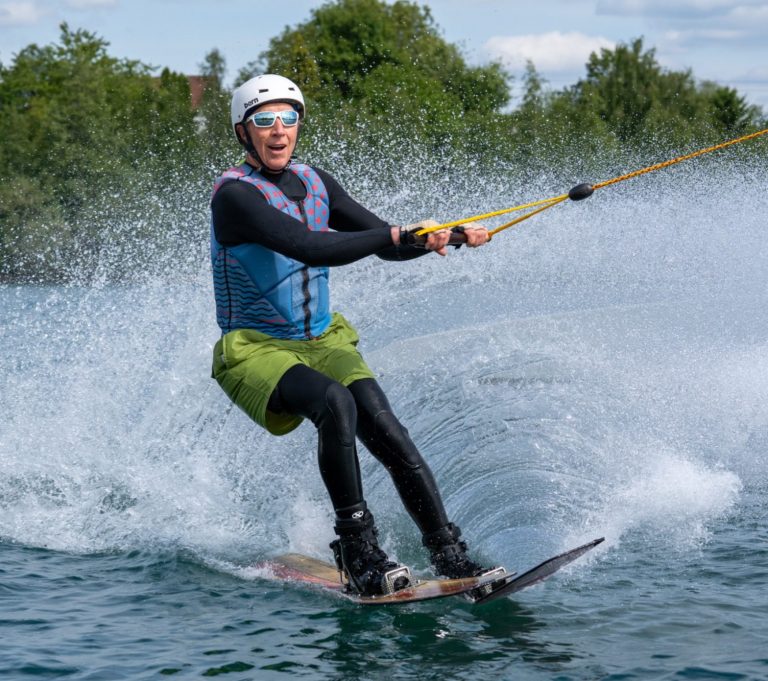 Person beim Wasserskifahren auf einem See, spritzendes Wasser um ihn herum.