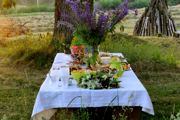 Midsommar Special Ein festlich gedeckter Tisch im Freien mit bunten Speisen und einer Blumenvase.