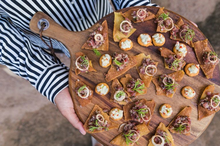 All White Party Ein Holzbrett mit verschiedenen kreativen Häppchen und Canapés, dekoriert mit Kräutern.