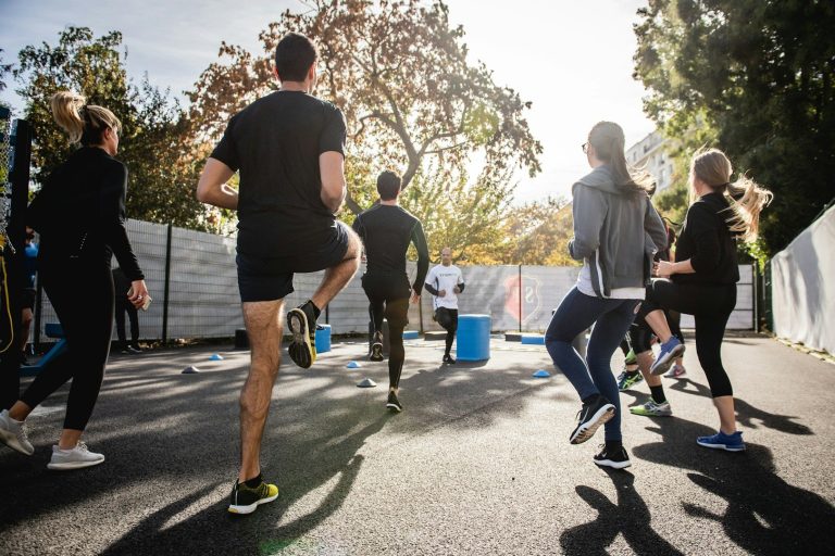 Sportstunde am See Gruppe von Menschen beim Laufen im Freien, umgeben von Bäumen und Sonnenschein.
