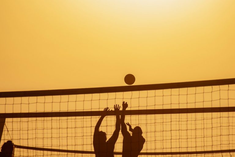 Volleyballturnier Silhouetten von zwei Spielern, die beim Volleyball einen Ball über das Netz schlagen.