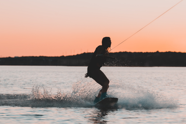 Event "Female Only Event" Person beim Wakeboarden vor einem rosa-orangefarbenen Sonnenuntergang.