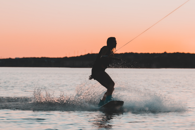 Event "Female Only Event" Person wakeboardet beim Sonnenuntergang auf einem ruhigen Gewässer.