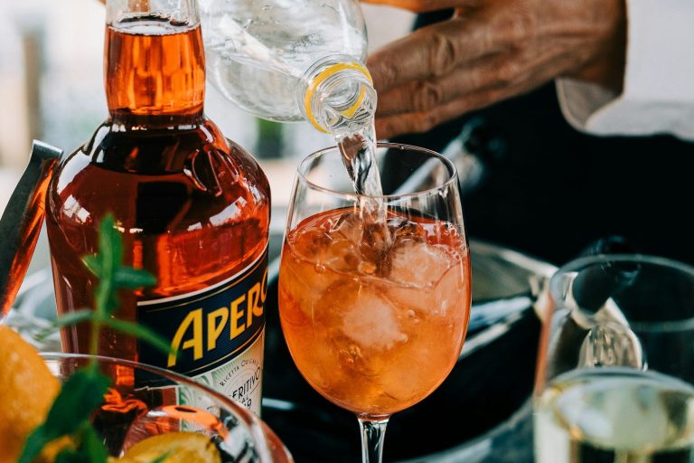 Happy Hour Ein Glas mit Aperol Spritz, Eiswürfeln und Sprudelwasser, umgeben von Zutaten.