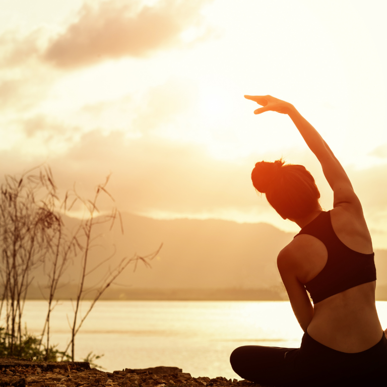 Frau macht Yoga im Sonnenuntergang am Wasser, mit Blick auf die Berge.
