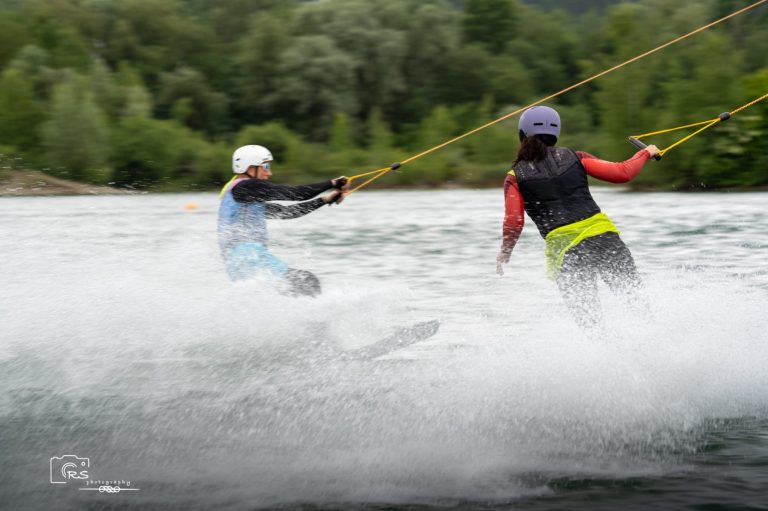 Sommerferien Kick-Off Zwei Personen wakeboarden auf einem Fluss, umgeben von Bäumen und Nebelschwaden.