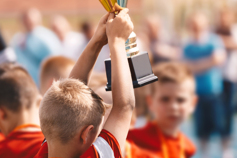 Seifenkistenrennen Ein Junge hebt einen Pokal hoch, umgeben von weiteren Kindern und Erwachsenen.
