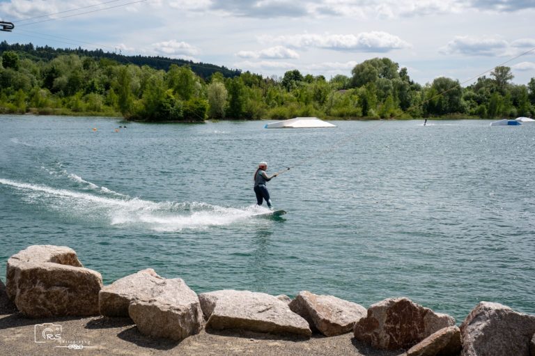 Schier Boards Testtag Person auf dem Wasser mit einem Wakeboard, umgeben von Bäumen und einem klaren Himmel.