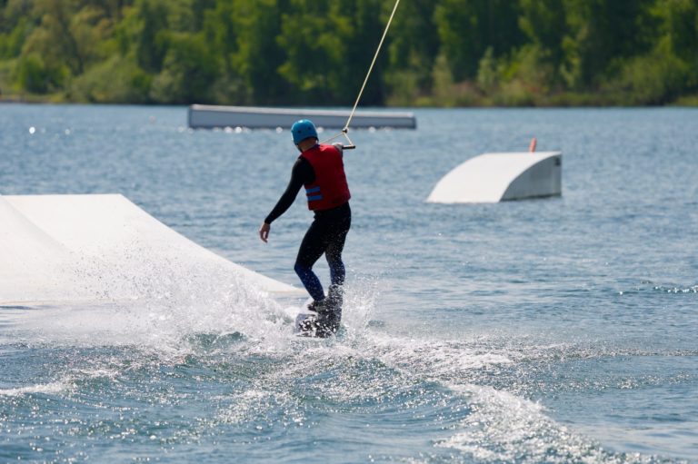 Kostümwettbewerb Person fährt auf einem Wakeboard über das Wasser, umgeben von Natur.